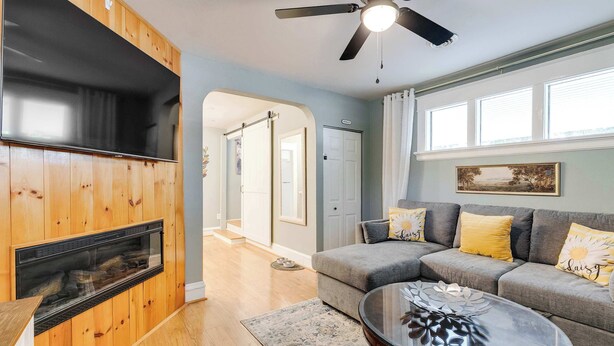 Ein Wohnzimmer mit Kamin, Deckenventilator, einer Couch mit Kissen, einem Couchtisch und einem Teppich.