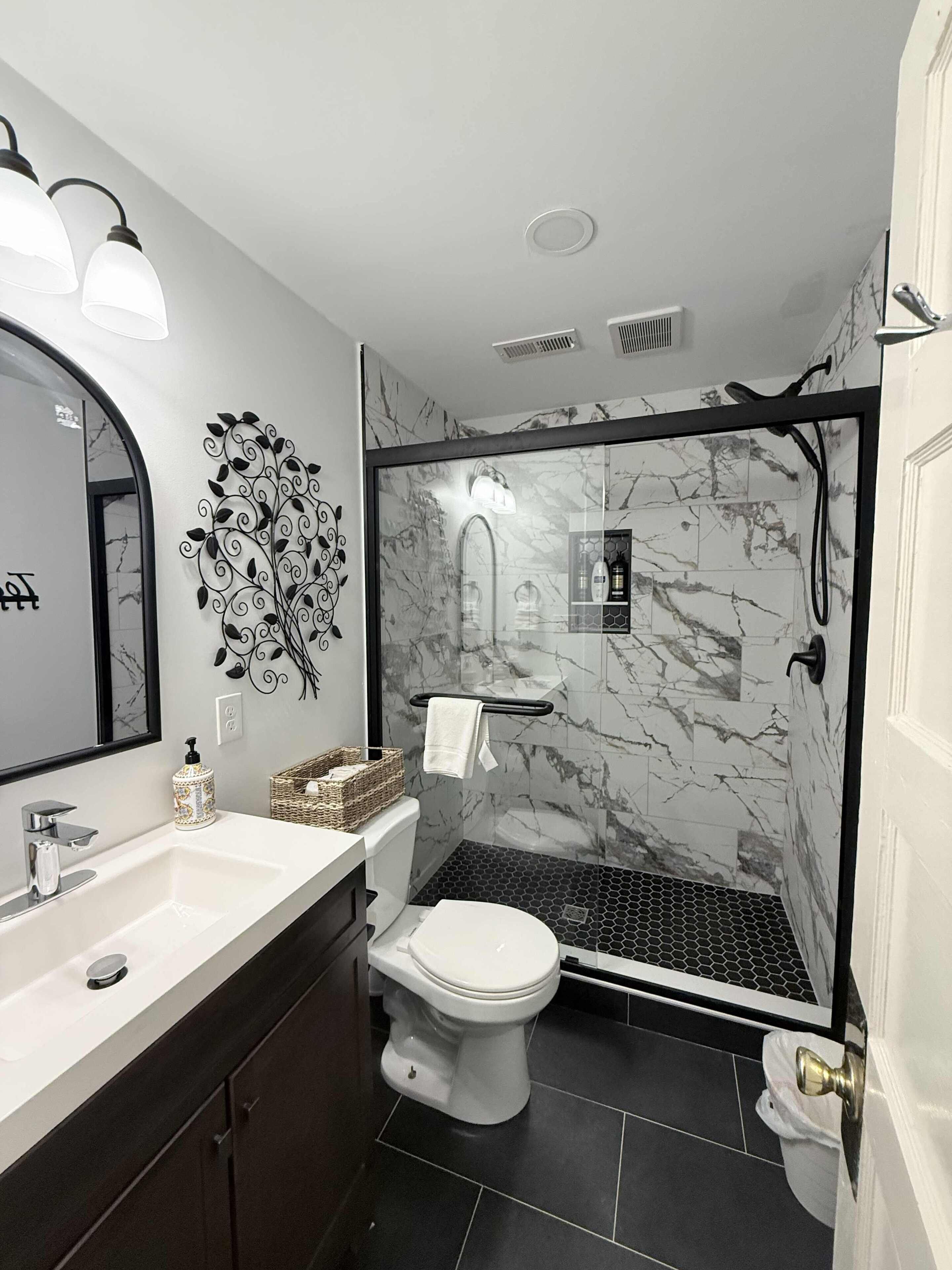 A modern bathroom with a marble shower, a toilet, and a sink with a mirror.. The Urban Cottage 4BR Private Family Retreat /Parking/fully fenced