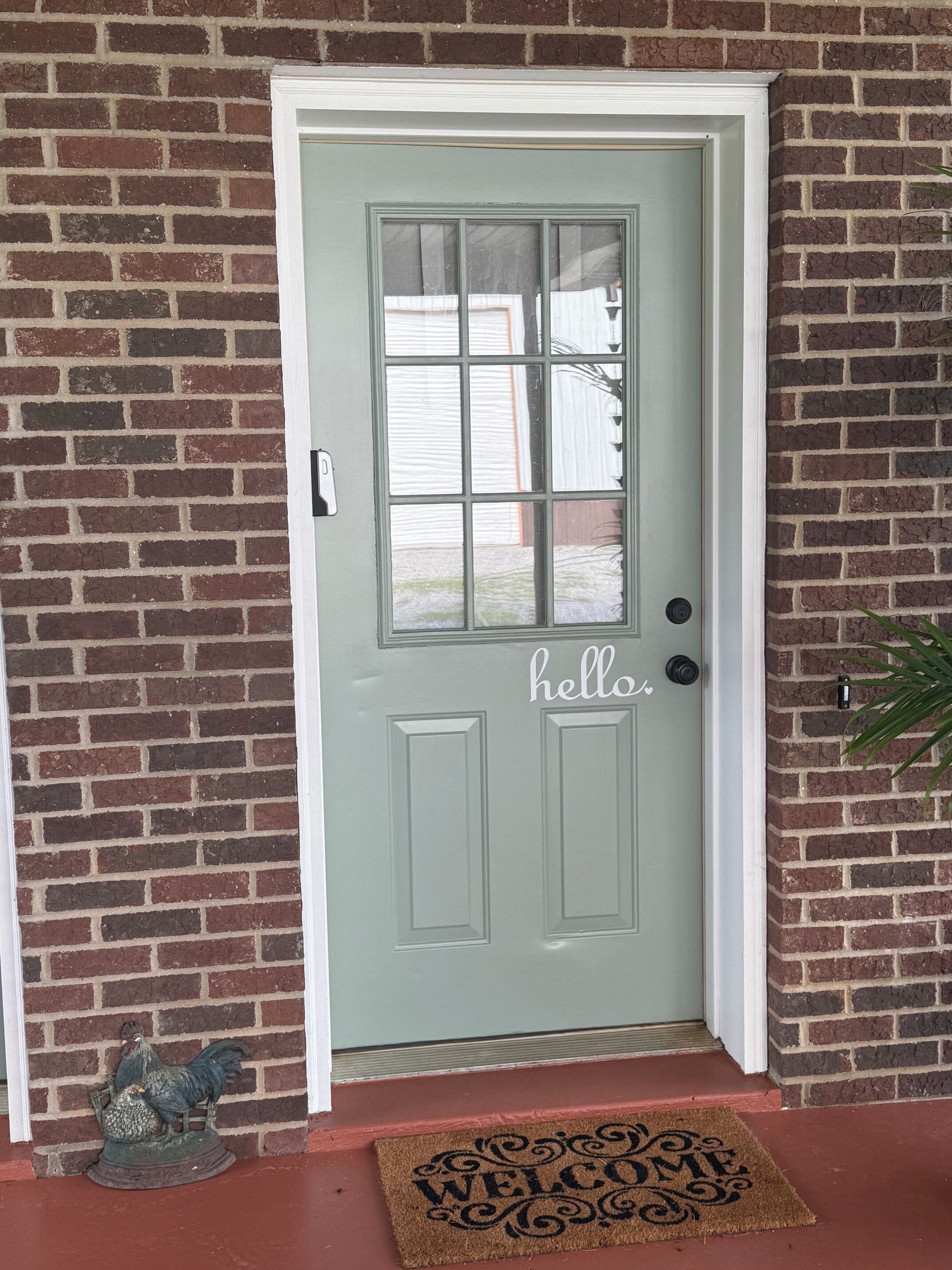 A door with a 'hello' sign, a doormat, and a small rooster decoration.