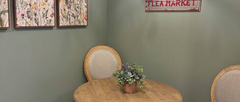 Un comedor con una mesa redonda de madera, dos sillas, una araña y tres obras de arte con motivos florales.