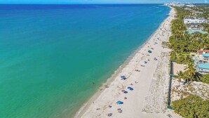 A beach with clear turquoise water, a sandy shore, and a row of buildings along the coastline.
