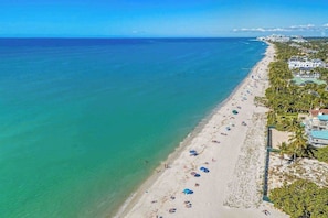 Ein Strand mit klarem türkisblauem Wasser, einem Sandstrand und einer Reihe von Gebäuden entlang der Küste.