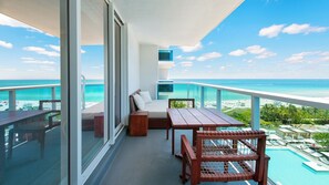 Ein Balkon mit einer Couch, einem Holztisch und einem Stuhl mit Blick auf einen Pool und einen Strand.