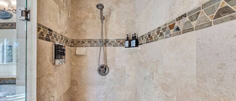 A shower with a handheld showerhead and a wall-mounted faucet, a glass shower door, and a tiled shower area with a decorative border.