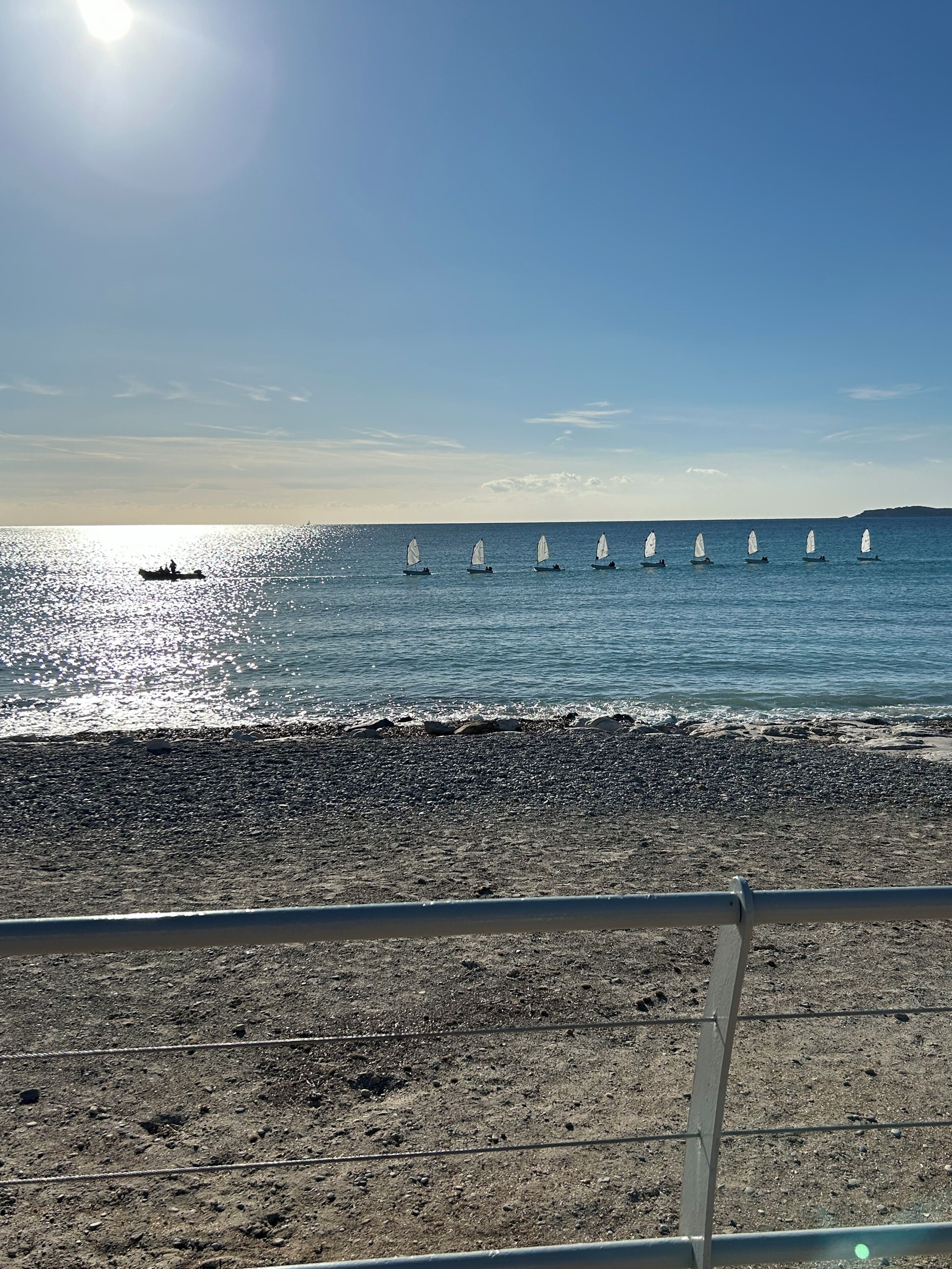 Een strand met zeilboten, een heldere lucht en een landmassa in de verte.