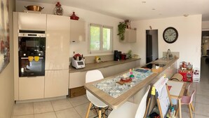 A modern kitchen with a built-in oven, a coffee machine, and a dining area with a table and chairs. - Family home with a pool near the village, close to the beaches (Saint-Cyr-sur-Mer)