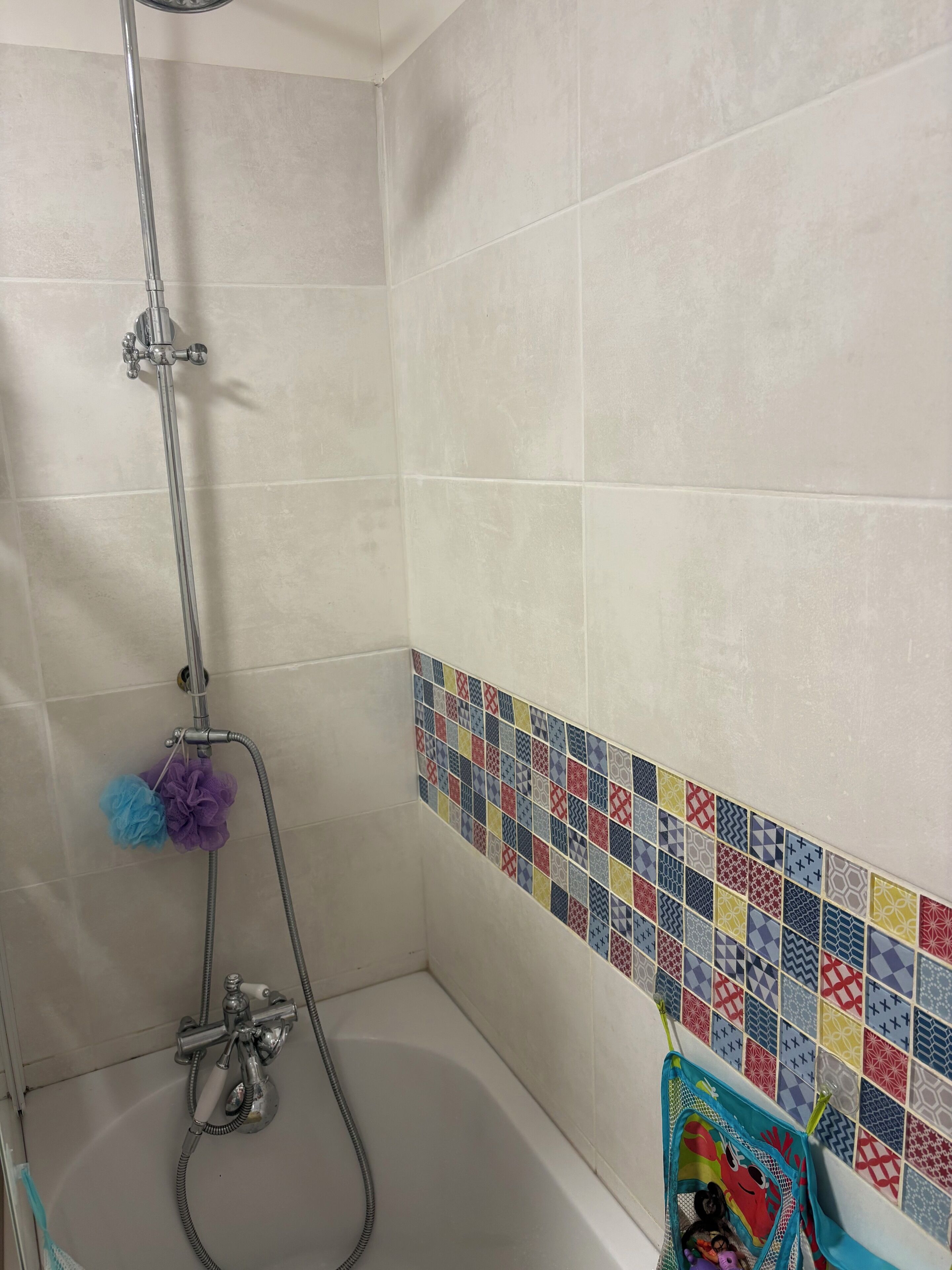 A shower with a chrome faucet and a handheld showerhead, a bathtub with a hose, and a colorful tile border.