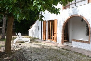 Edifici de color blanc amb un arc de rajola i portes de fusta, un arbre i seients relaxants blancs al primer pla.