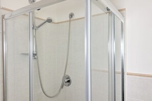 Dutxa tancada amb vidre, amb plat de roba de mà i un braç de dutxa fixat a la paret.