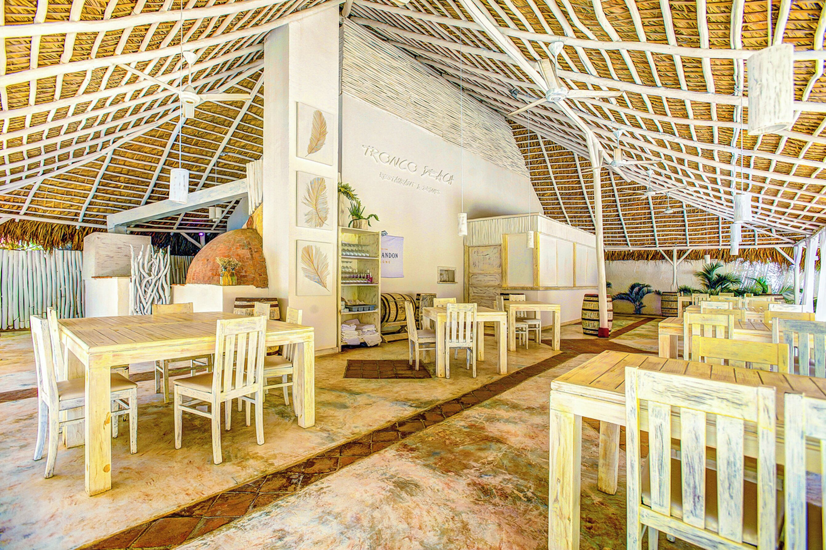 Un interno spazioso con soffitto alto, tavoli e sedie in legno e una zona centrale con un bancone e scaffali.