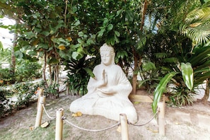 Eine steinerne Buddha-Statue, umgeben von üppigem Grün und einer Seilsperre.