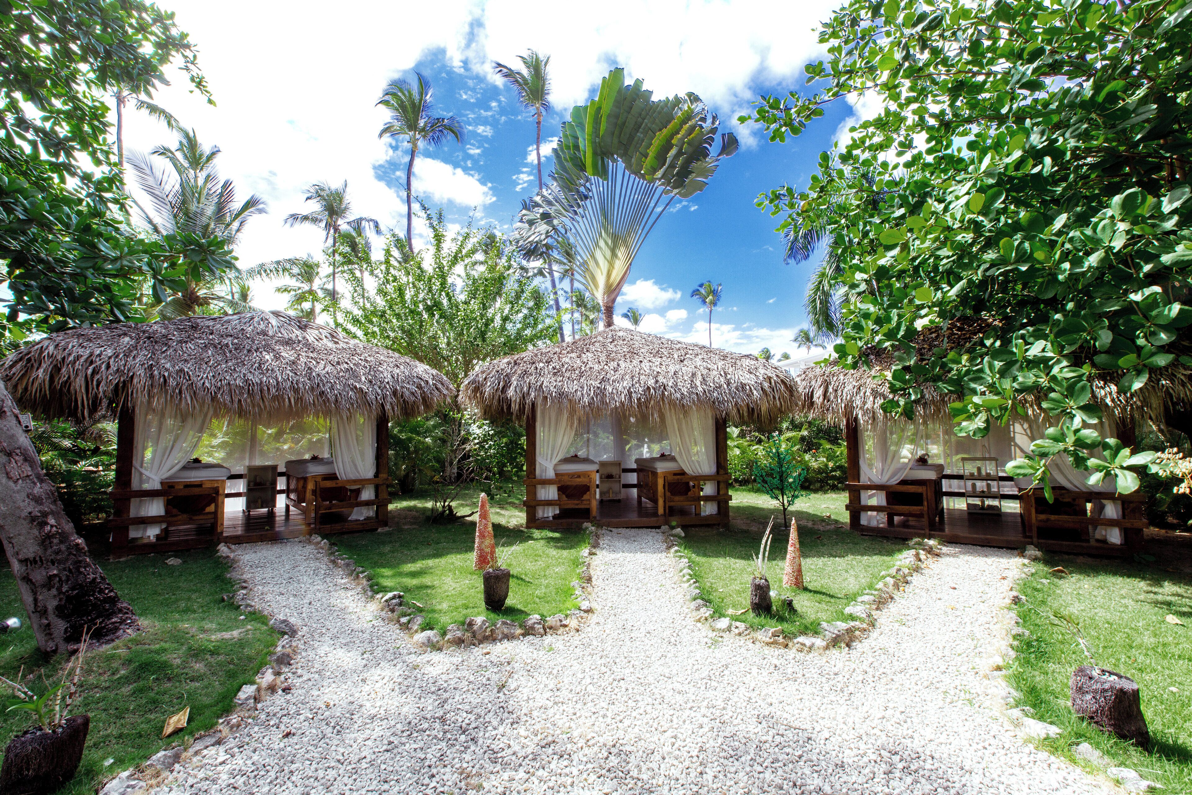 A tropical resort with thatched-roof huts, a gravel pathway, and lush greenery.