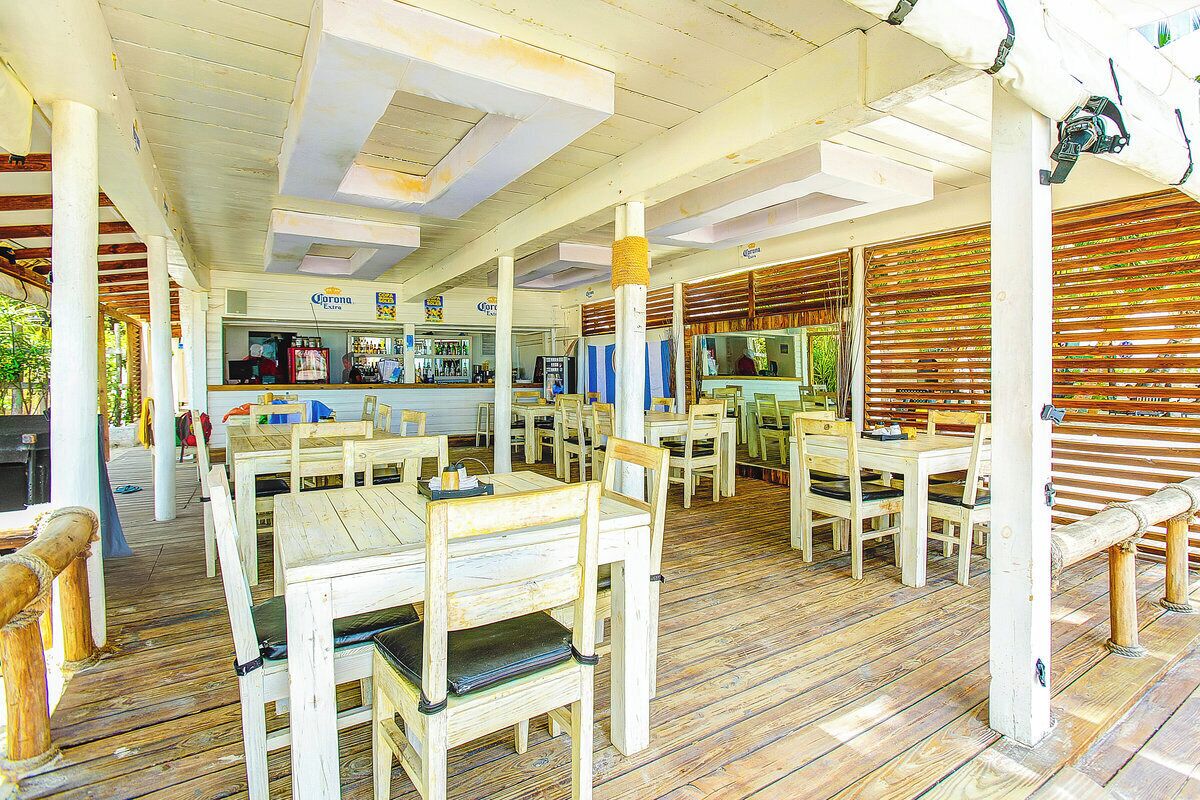 An outdoor restaurant with wooden tables and chairs, a bar area, and a covered seating area.