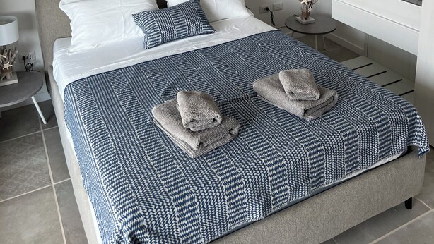 A bedroom with a bed, bedside table, lamp, and a hanging light fixture. - The View 108 - Stylish apartment near the beach in Baja Sardinia (Baja Sardinia)