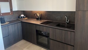 A modern kitchen with dark wood cabinets, a black countertop, a built-in oven, and a double sink. - The View 108 - Stylish apartment near the beach in Baja Sardinia (Baja Sardinia)