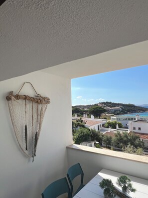Un balcon donnant sur une ville côtière, un décor suspendu en forme de filet et une table avec des chaises.