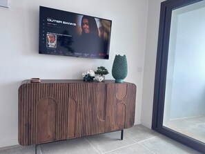 Ein modernes Wohnzimmer mit flachbildfernseher an der Wand, einem Holzkonsolentisch mit Dekoration und einem großen Fenster.