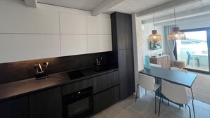 A modern kitchen with dark cabinetry, a built-in oven, and a dining area with a table and chairs. - The View 108 - Stylish apartment near the beach in Baja Sardinia (Baja Sardinia)