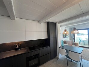 Une cuisine moderne avec des meubles de couleur sombre, un four encastré et un coin repas comprenant une table et des chaises.