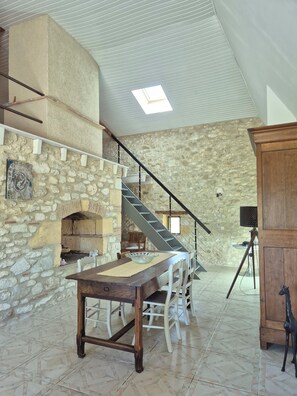 A stone-walled room with a fireplace, a dining table with chairs, a staircase, and a wooden cabinet. - Quiet, unoverlooked country house with private saltwater pool (Lacaussade)