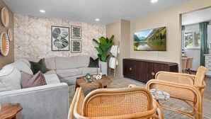 A living room with a sofa, two wicker chairs, a coffee table, a TV, and a large plant. - Hot Tub, Sauna & Game Room Mountain-View Home (Westminster)