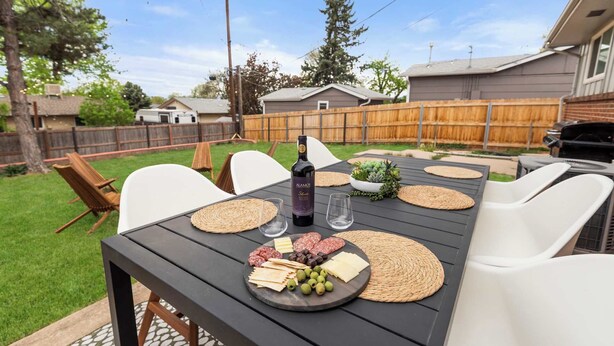 An outdoor patio with a table set for a meal, including a bottle of wine, cheese, and olives. - Hot Tub, Sauna & Game Room Mountain-View Home (Westminster)