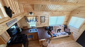 A compact cabin with a kitchen, dining area, and a bed with a bear-themed headboard.