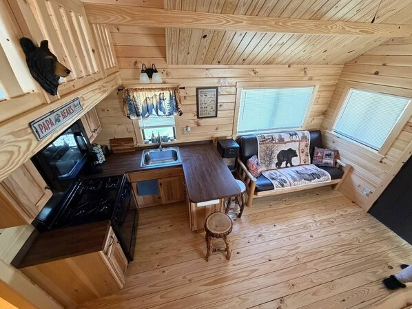 A compact cabin with a kitchen, dining area, and a bed with a bear-themed headboard.
