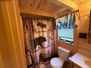 A bathroom with a wooden interior, a toilet, a sink, and a window with blinds.