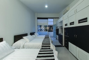 A hotel room with two beds, a large window, a kitchenette, and a wardrobe.