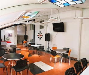 A conference room with tables and chairs, a flat-screen TV mounted on the wall, and a ceiling with skylights.