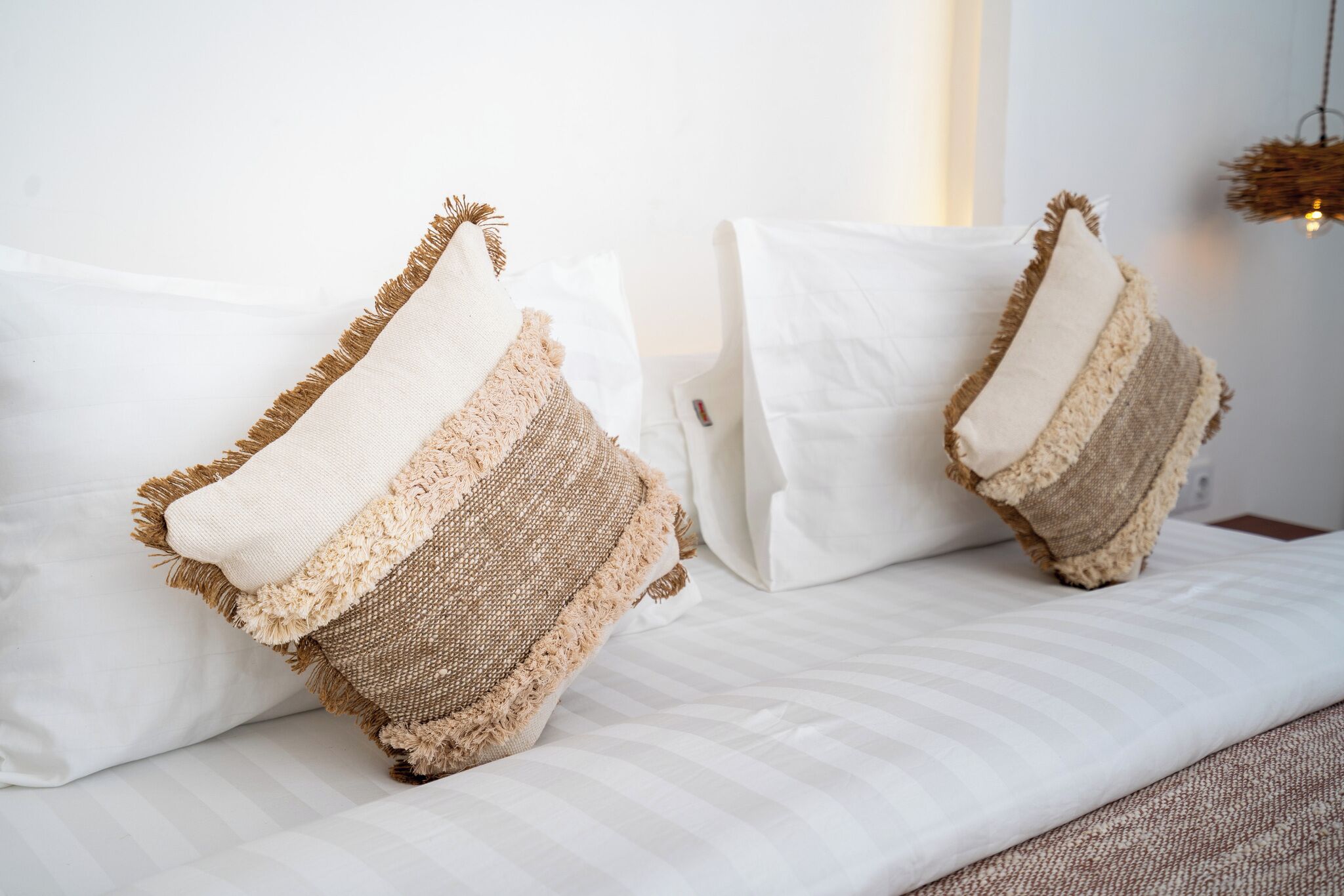 A bed with two pillows, a white wall, and a hanging light fixture.