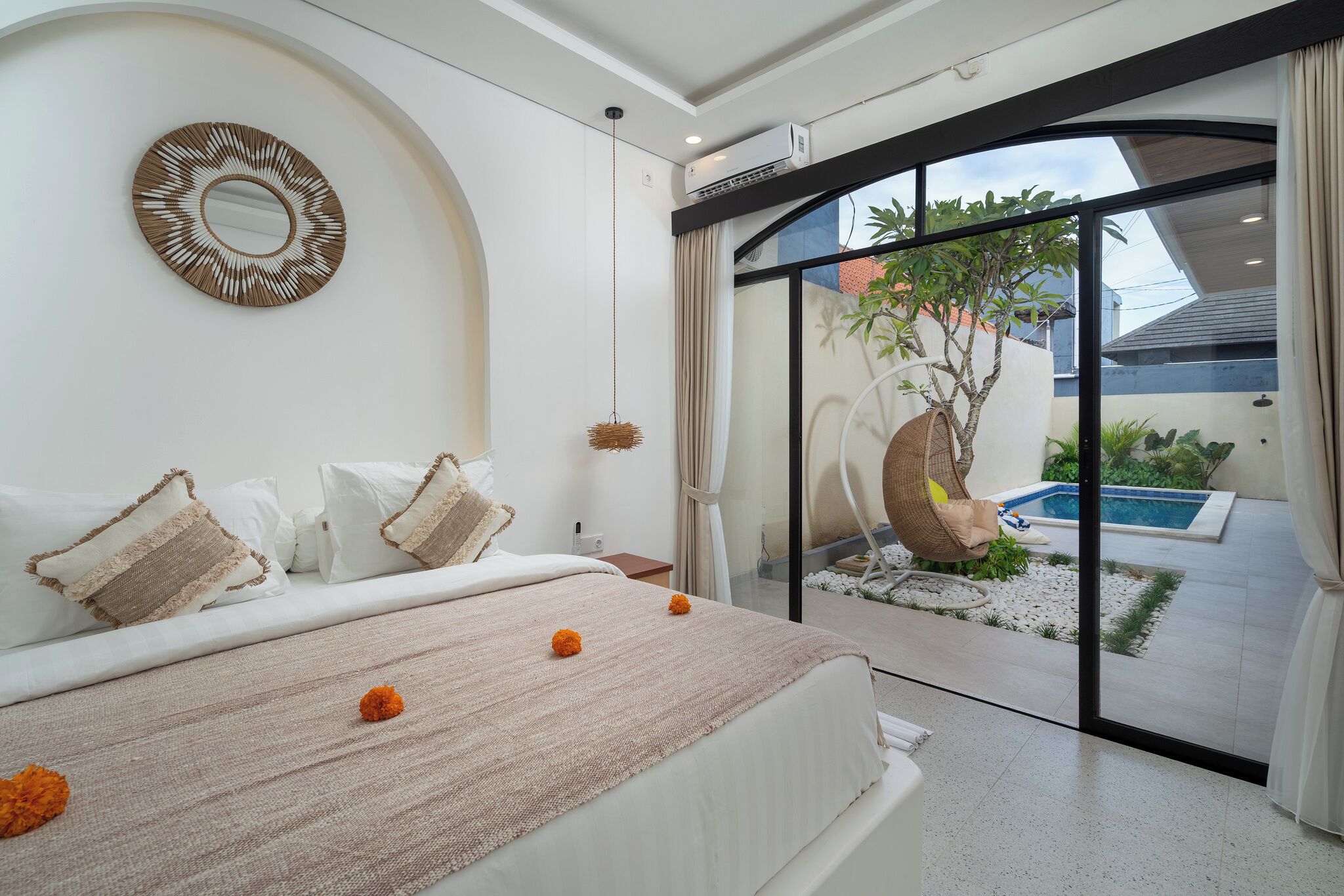 A bedroom with a bed, pillows, a hanging basket, and a view of an outdoor swimming pool and garden.