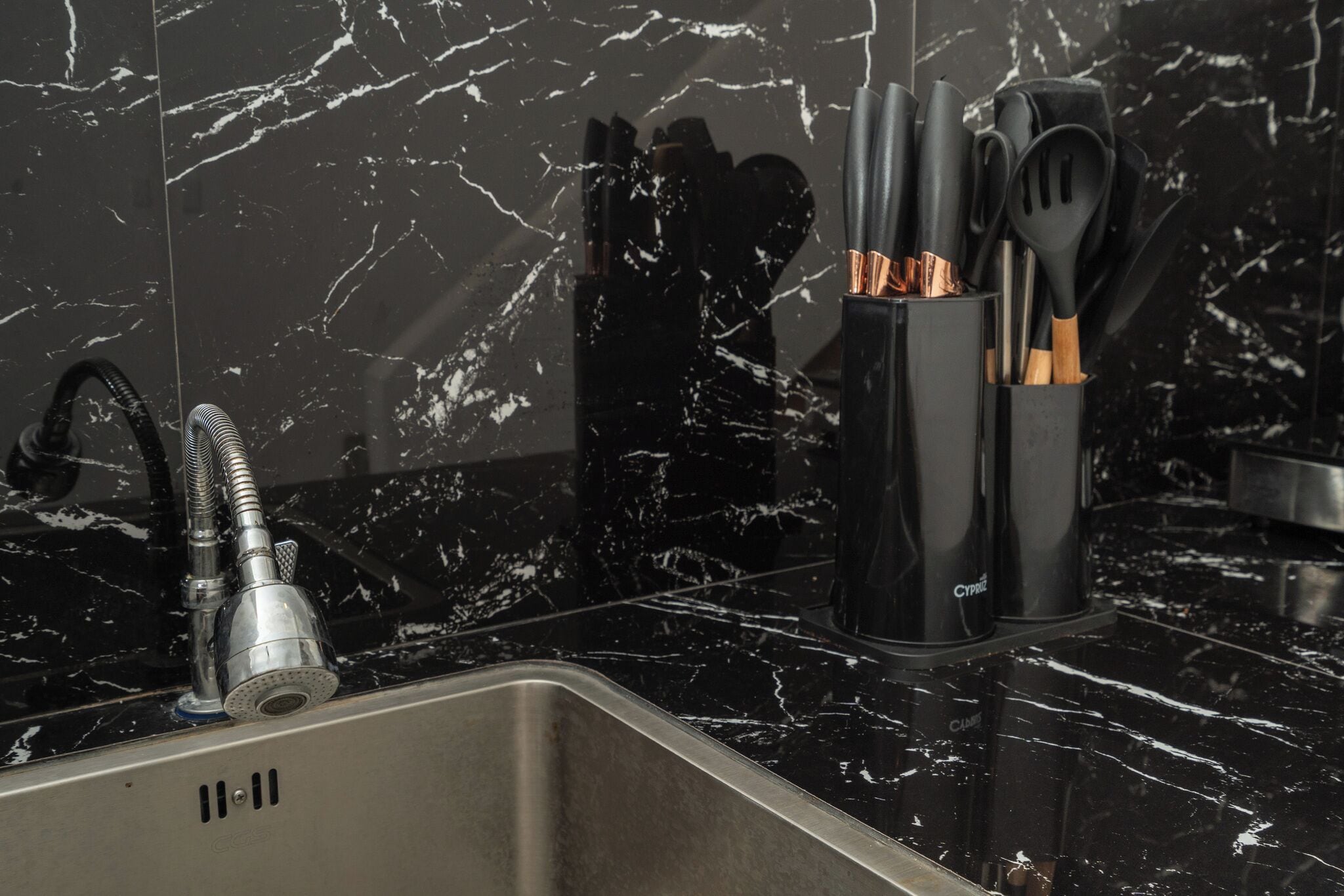 A kitchen with a black marble countertop, a stainless steel sink, and a black utensil holder with copper handles.