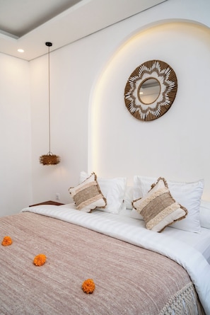 A bedroom with a bed, white pillows, a brown woven headboard, a hanging light fixture, and a circular mirror. - Cozzy  Ayura Villa Legian (denpasar)
