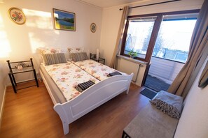 A bedroom with a double bed, a bedside table, a radiator, a window with curtains, and a picture on the wall.