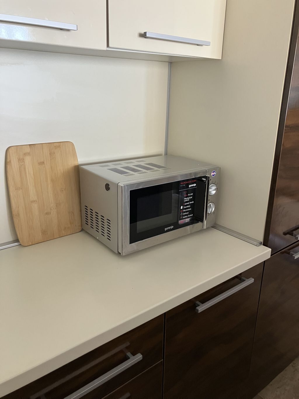 Eine Mikrowelle steht auf einer Küchenarbeitsplatte, daneben ein Schneidebrett aus Holz.