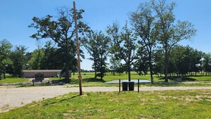 A grassy field with trees, a bench, and a building in the background. - BEAUTIFUL LAKE SHELBYVILLE CAMPING SITE ALONG SIDE STOCKED FISHING PONDS SITE #2 (Lakewood)