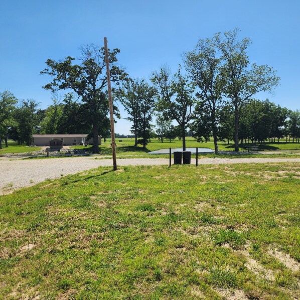 A grassy field with trees, a bench, and a building in the background.