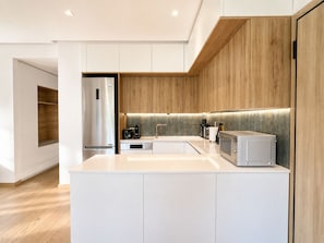 A modern kitchen with white cabinetry, a stainless steel refrigerator, a built-in microwave, and a wooden accent wall.
