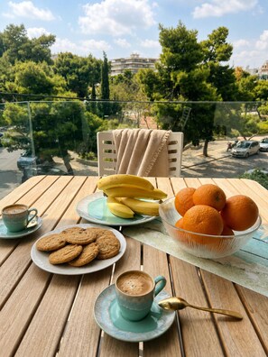 A table with a plate of cookies, a bowl of oranges, a plate of bananas, and a cup of coffee.