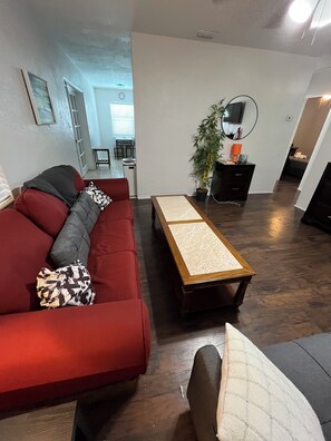 A living room with a red sofa, a wooden coffee table, a potted plant, and a television. - Cute Pool home in Jungle Terrace - 3/1  fast WiFi, 35 days minimu - 10' to beach (St. Petersburg)