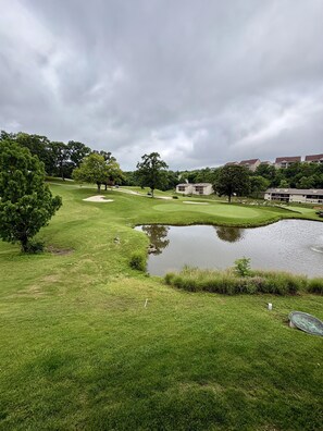 Ein Golfplatz mit Teich, Bäumen und Wohnhäusern im Hintergrund.