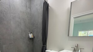 A bathroom with a shower, toilet, sink, and cabinet. - The Still Waters Cottage (Evart)