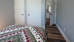 A bedroom with a large bed, two white doors, and a hallway leading to a bathroom. - The Still Waters Cottage (Evart)