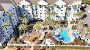 A multi-story hotel with a swimming pool, palm trees, and a tennis court. - Cozy 1-bedroom apartment in charming Orlando (Orlando)