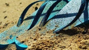 Een blauwe slippers op zand.