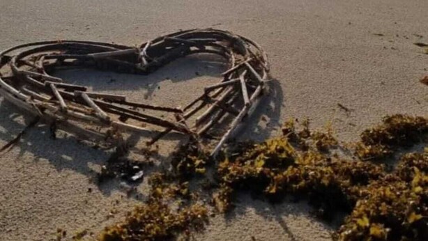 Een hartvormige compositie van stokken op een strand, met golven op de achtergrond.