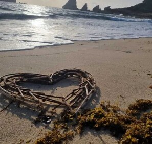 A heart-shaped arrangement of sticks on a beach with waves in the background. - BUNGALOW DE SAINT JACQUES (Saint-François)