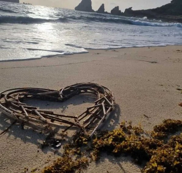 A heart-shaped arrangement of sticks on a beach with waves in the background. - BUNGALOW DE SAINT JACQUES (Saint-François)